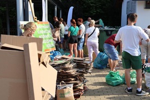 zdjęcie przedstawia uczestników akcji wymiany surowców na sadzonki, widoczne są kartony, zielone worki na szkło, plakat promujący akcję