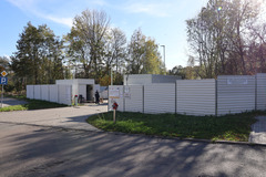 Na zdjęciu widoczny jest ogrodzenie i wjazd do PSZOK, W tle widać drzewa.